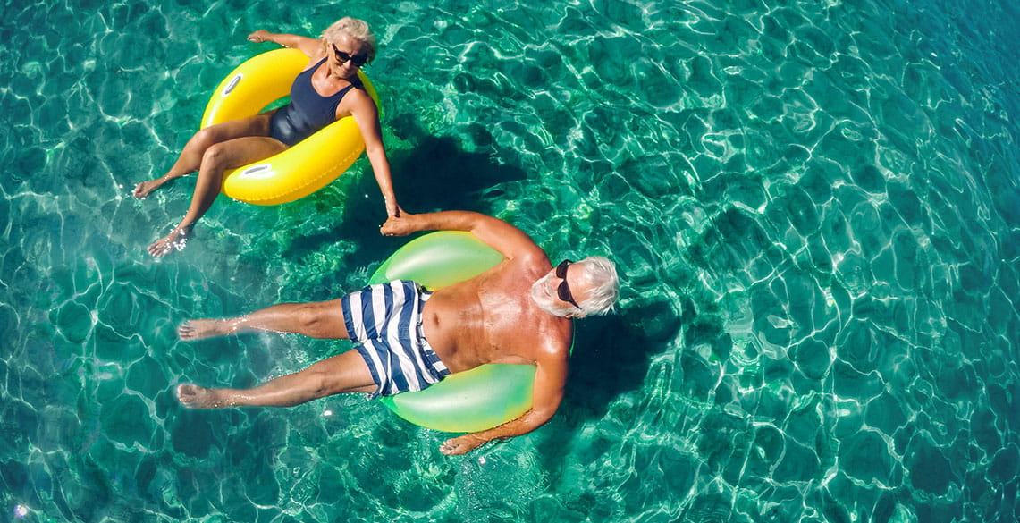 two older people floating in floating rings on a wide green ocean