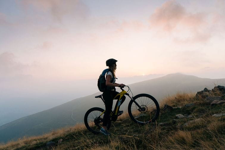 Female mountain biker pauses in alpine track, sunrise